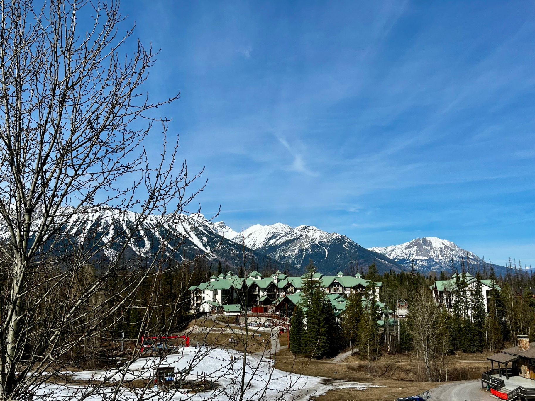 Snow-capped Canadian Rockies rising behind a green-roofed mountain resort village in early spring
